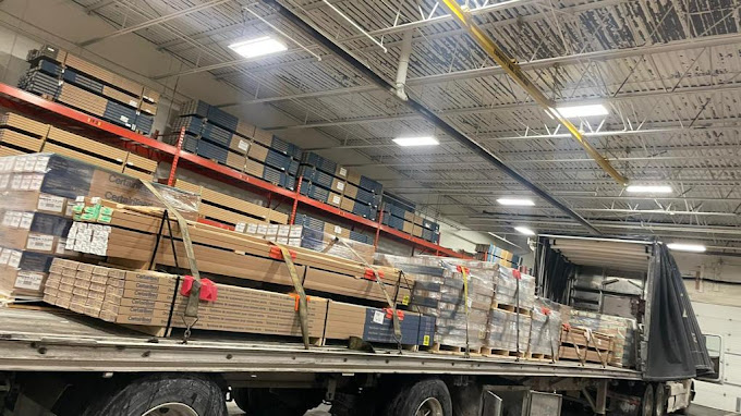 Flatbed truck loaded with secured pallets inside a warehouse.