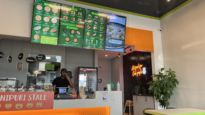 A modern restaurant with a green menu board, a neon sign, and a staff member at the counter.