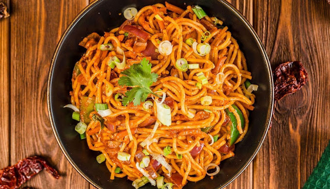 A bowl of spicy stir-fried noodles garnished with herbs and vegetables.